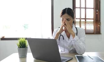 doctora sosteniendo un estetoscopio sentado con dolor de cabeza por estrés de una computadora portátil sobre su trabajo y trabajo en el hospital. foto