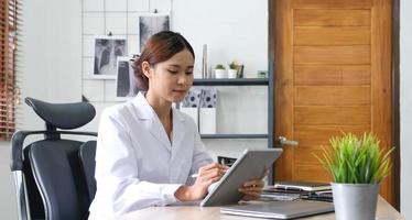 asian female doctor with laptop computer in her office. Friendly medical professional with tablet computer in clinic. photo