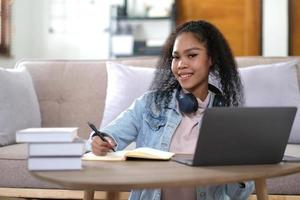 retrato de una estudiante feliz con piel oscura sonriendo a la cámara. alegre chica hipster afroamericana disfrutando del aprendizaje electrónico y la preparación para el trabajo del curso foto