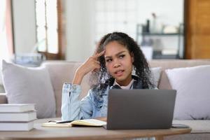 Exhausted female student feeling headache from problems with university course work connected to wifi for browsing informative websites, unhappy dark skinned woman tired from e learning on laptop photo