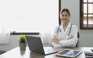 Portrait of young asian female doctor smiling and looking at camera sitting in examination room. photo