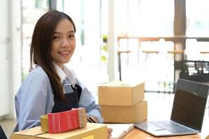 Retrato de mujer joven asiática SM trabajando con una caja en casa el lugar de trabajo.Propietario de una pequeña empresa de inicio, pequeña empresa emprendedora o empresa independiente en línea y concepto de entrega. foto