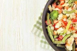 Mixture of frozen vegetables on white wooden background photo