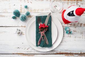 Christmas table setting with white dishware, silverware and red and green decorations on white wooden background. Top view. photo