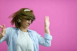 brunette lady in black glasses dancing and   listening music isolate on pink background photo