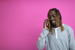 chico afro usa un teléfono mientras posa frente a un fondo rosa. foto