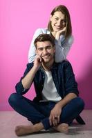 couple sitting on the floor while posing in front of a pink background photo