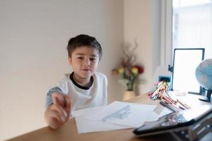 School kid using grey colour pen drawing or sketching on paper,Portrait  boy siting alone and looking out with thinking face, ,Child enjoy art and craft activity at home on weekend,Education concept photo