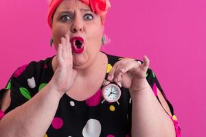 retrato de una joven de talla grande con las manos sonrientes sostiene un reloj de arena aislado en un fondo de color rosa. foto