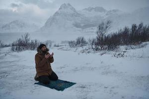 Muslim traveler praying in cold snowy winter day photo