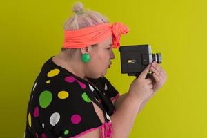 plus size smiling woman with funny emotional face expression with vintage camera in dress isolated on green background, traveler on vacation, summer fashion style, excited tourist. photo