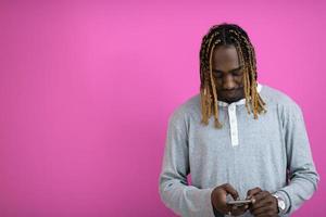 afro guy uses a phone while posing in front of a pink background. photo