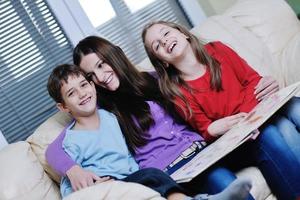 mamá joven juega con sus hijos en casa y lee libros foto