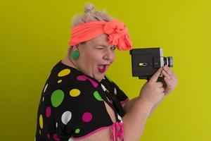 plus size smiling woman with funny emotional face expression with vintage camera in dress isolated on green background, traveler on vacation, summer fashion style, excited tourist. photo