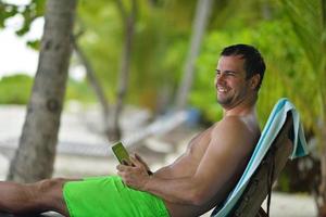 hombre relajándose y usando tableta en la playa foto