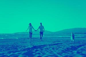 couple with dog having fun on beach on autmun day photo