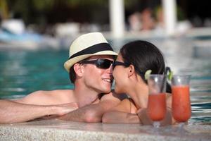 feliz pareja joven relajarse y tomar una bebida fresca junto a la piscina