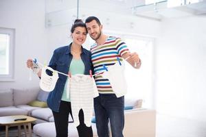 young couple holding baby bodysuits at home photo