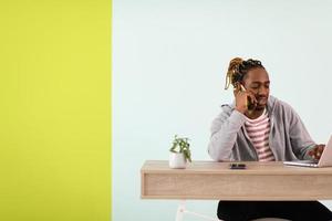 afro young man sits in his home office during a pandemic and uses the phone photo