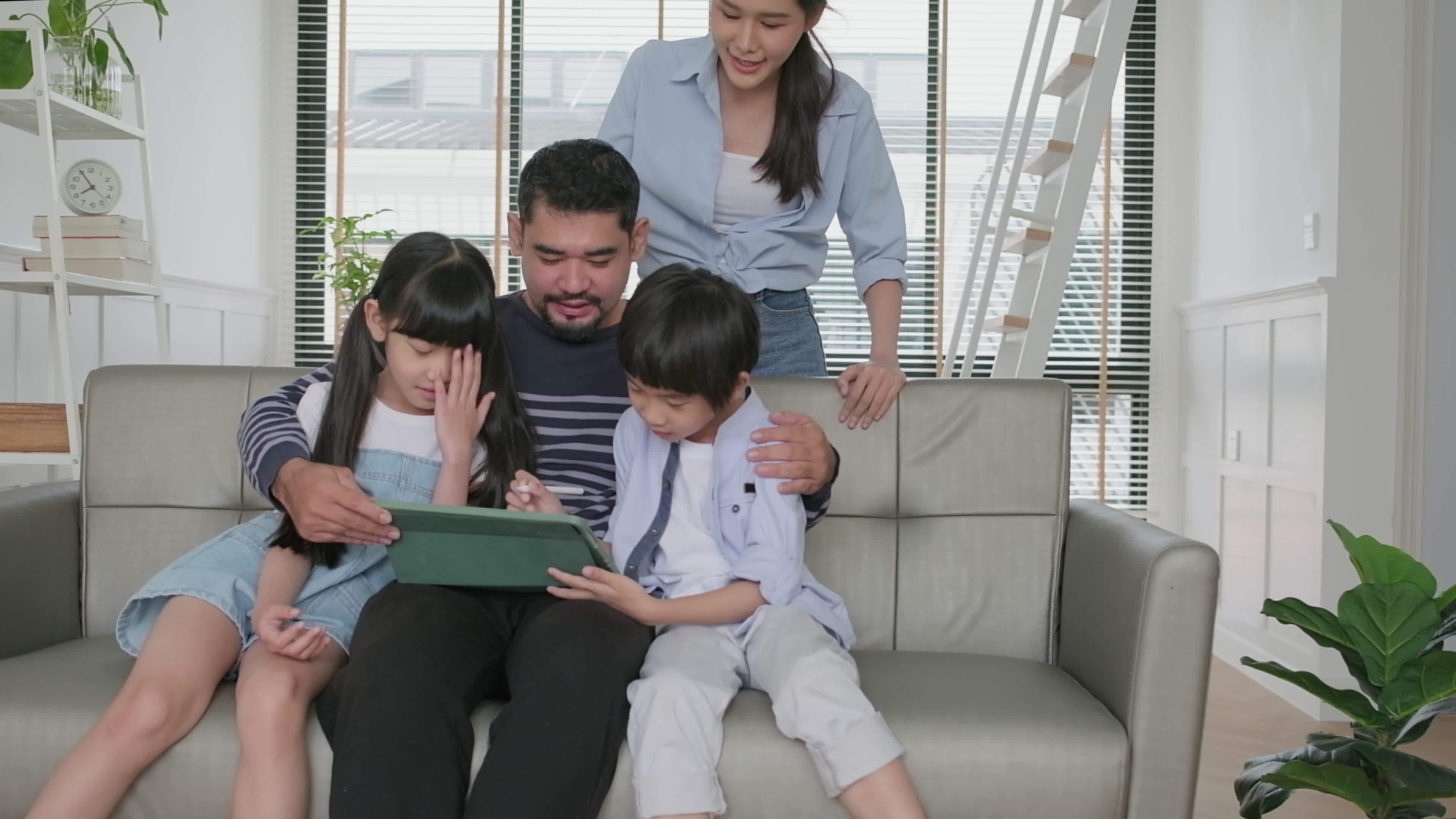 Happy Asian Thai family, parents, and children have fun using digital tablet together on sofa in home living room, a lovely leisure weekend, and domestic wellbeing lifestyle with internet technology. photo