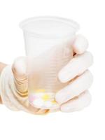 gloved hand holding plastic cup with pills photo