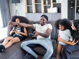 Family father dad male man and mother mom woman female son girl kid child happy lifestyle parent african american ethnicity joystick controller videogame people of group indoor living room sofa home photo