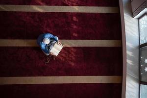 hombre musulmán rezando solo a alá dentro de la mezquita y leyendo el libro sagrado islámico foto