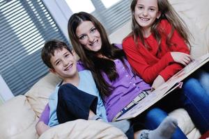 mamá joven juega con sus hijos en casa y lee libros foto