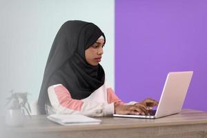 afro girl wearing a hijab thoughtfully sits in her home office and uses a laptop photo