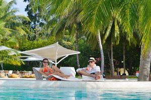 feliz pareja joven relajarse y tomar una bebida fresca junto a la piscina foto