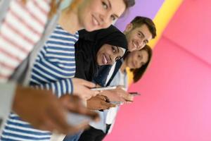 diverse teenagers use mobile devices while posing for a studio photo in front of a pink background