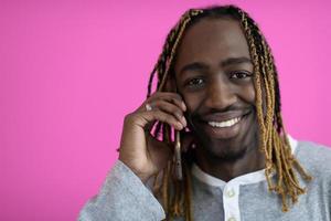 afro guy uses a phone while posing in front of a pink background. photo