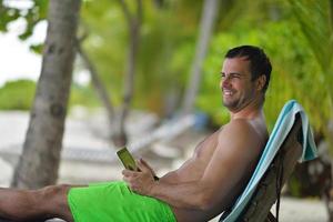 hombre relajándose y usando tableta en la playa foto