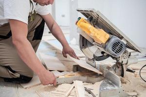 Man cutting laminate floor plank with electrical circular saw photo