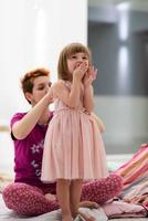 young mother helping daughter while putting on a dress photo