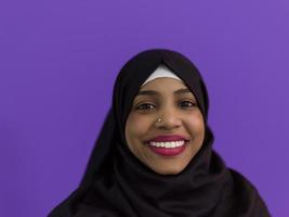 retrato de una mujer musulmana africana con hiyab y ropa musulmana tradicional posando frente a un fondo morado foto