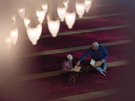 father and son in mosque praying and reading holly book quran together photo