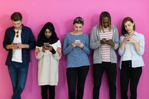 diverse teenagers use mobile devices while posing for a studio photo in front of a pink background