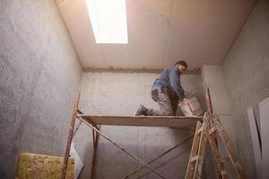 trabajador de la construcción enyesado en el techo de yeso foto