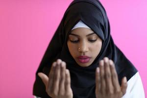 Modern African Muslim woman makes traditional prayer to God, keeps hands in praying gesture, wears traditional white clothes photo