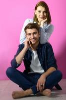 couple sitting on the floor while posing in front of a pink background photo