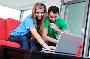 una pareja feliz se divierte y trabaja en una laptop en casa foto