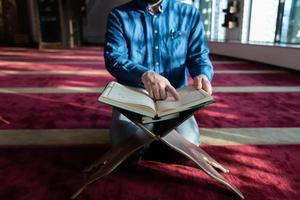 hombre musulmán rezando solo a alá dentro de la mezquita y leyendo el libro sagrado islámico foto