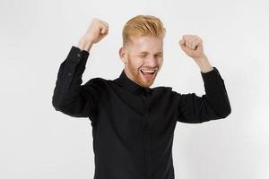 Reach the goal concept. Happy excited shock young guy entrepreneur isolated on gray background. Copy space. Close up Successful Redheaded man with red beard in stylish black shirt. Positive smart male photo