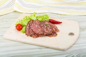 Sliced salami on wooden board and wooden background photo