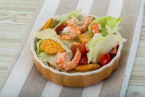 Caesar salad with shrimps in a bowl on wooden background photo