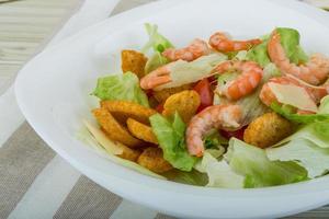 Caesar salad with shrimps in a bowl on wooden background photo