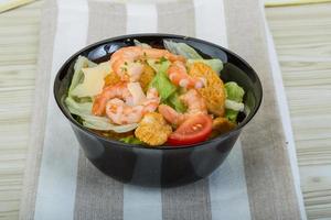 Caesar salad with shrimps in a bowl on wooden background photo