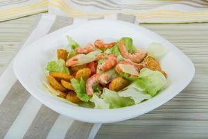 Caesar salad with shrimps in a bowl on wooden background photo