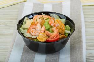 Caesar salad with shrimps in a bowl on wooden background photo